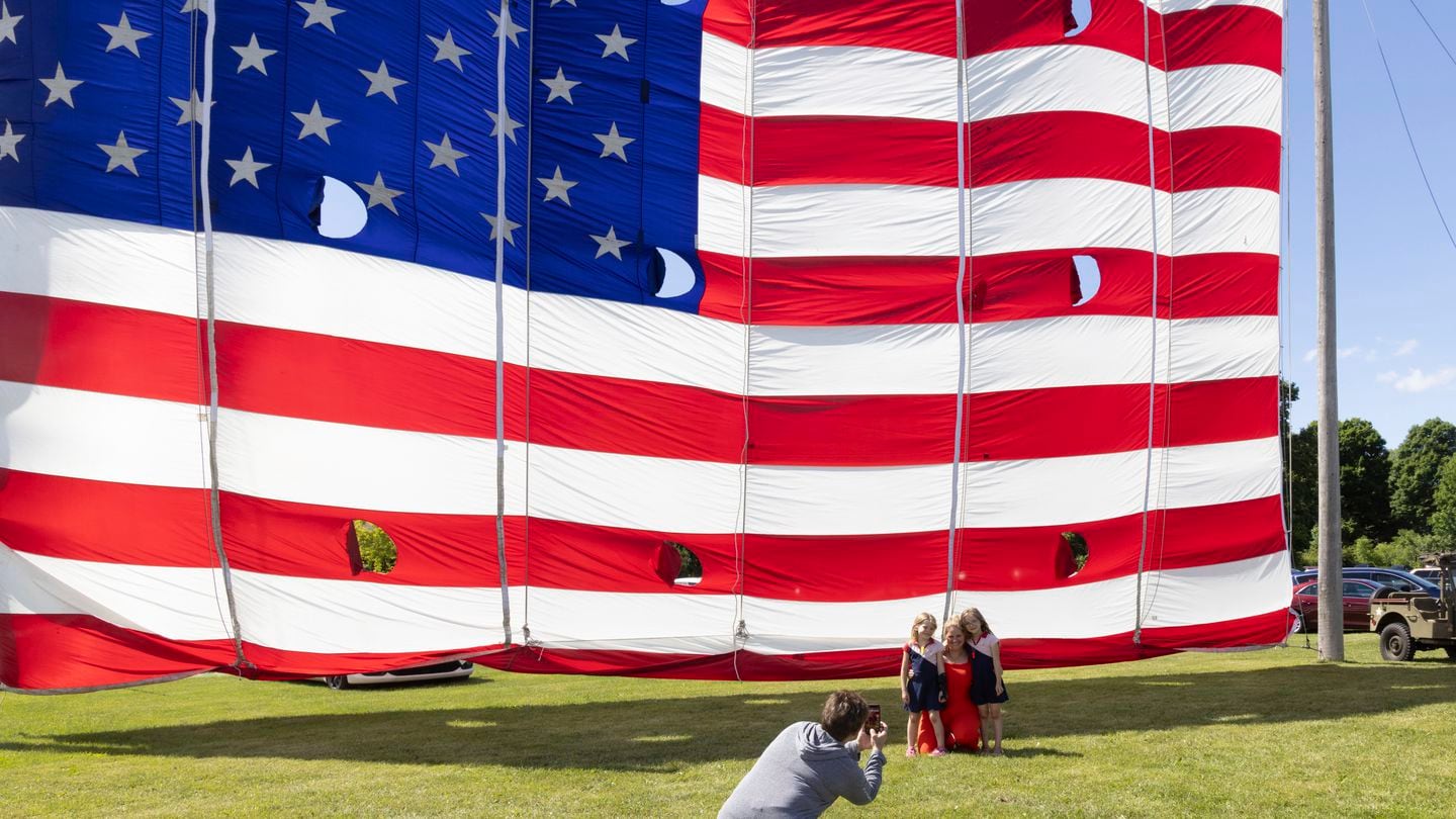 Brook Nugent poses with her twin daughters Maisie, left, and Sabrina, right, in front of a giant flag on display outside the National Flag Foundation in Waubeka, Wis., on June 9.