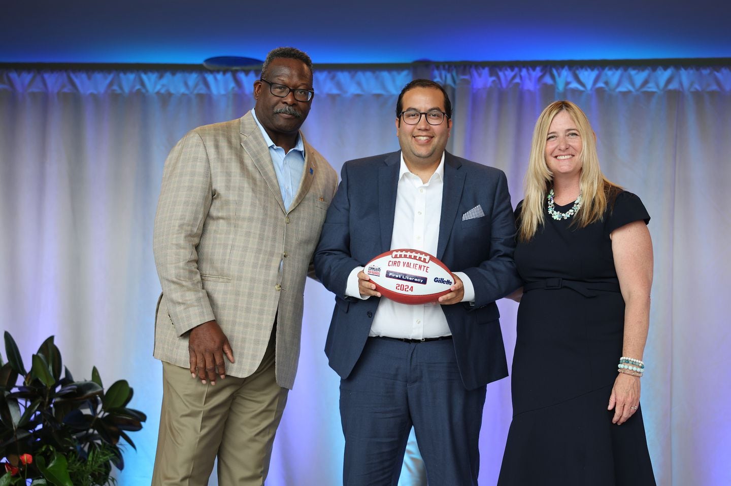 Patriots Pro Football Hall of Famer Andre Tippett (left) and Gillette’s Vice President of Communications & Community
Affairs, Global Grooming, Kara Buckley (right), congratulate Ciro Valiente from First Literacy of Boston for being selected as a
2024 Myra Kraft Community MVP Award winner.