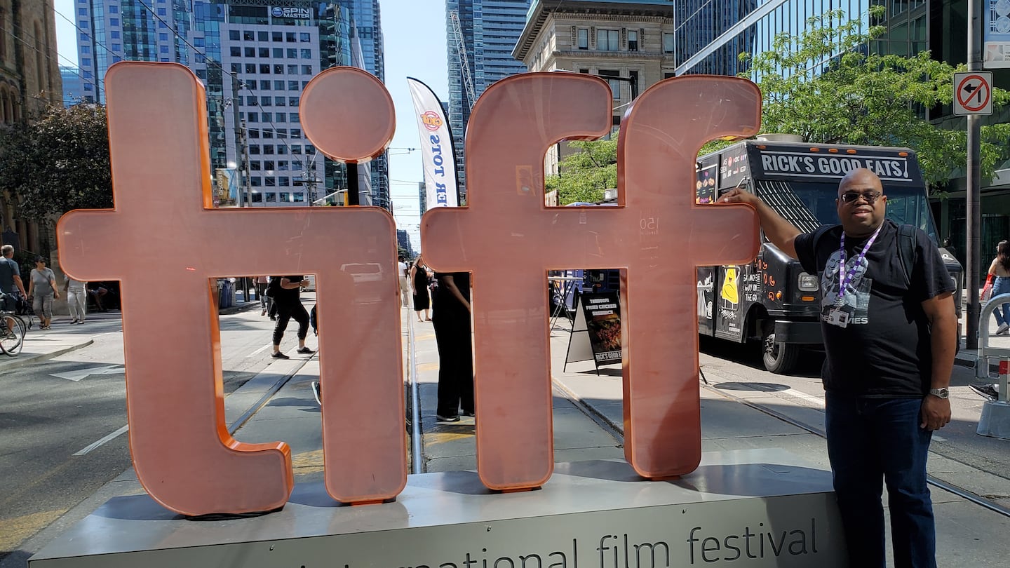 Boston Globe film critic Odie Henderson poses for a picture at a TIFF sign.