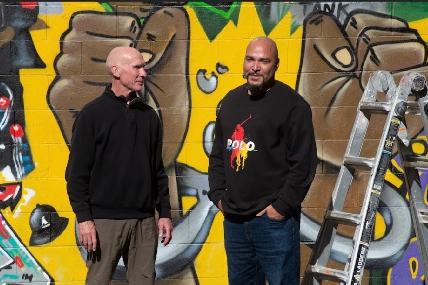 Former Boston police officer Paul Joyce, left, with the graffiti artist Alvin Colon in front of a mural in Norwood that Colon made for Joyce's new book, “It Started With the Hats: The Life Experiences of Boston’s Founding Street Gang Members."