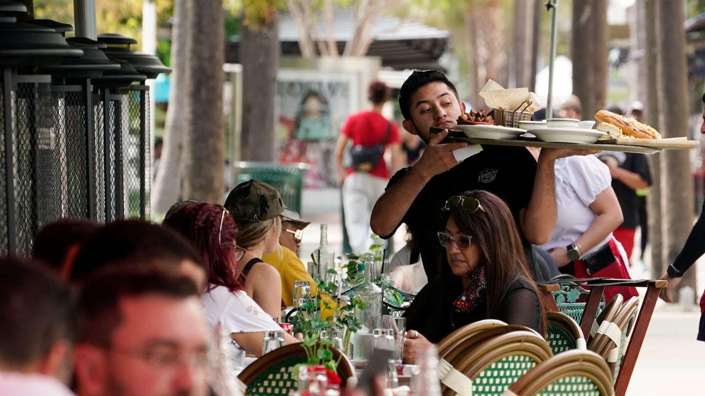 A waiter delivers food to patrons at a restaurant, in Miami Beach, Fla.