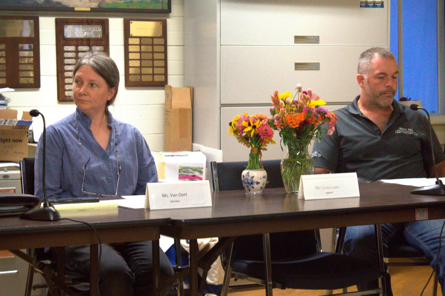 On Tuesday, Sept. 17, Pawlet Select Board members Jessica Van Oort and Rich Hulett sit next to the seat and flowers remembering slain Select Board member Brian Crossman Sr., who along with his wife and son were found shot to death in their home.