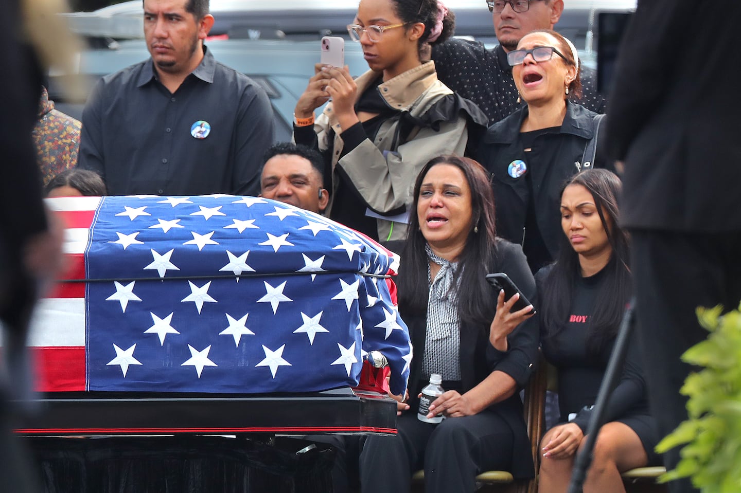 Sandra Garcia (center) sits with other family members as the flag-draped casket of her son, Enrique, is carried by Massachusetts State troopers. Enrique Delgado-Garcia’s funeral service was held Saturday outside at the Mercadante Funeral Home in Worcester.