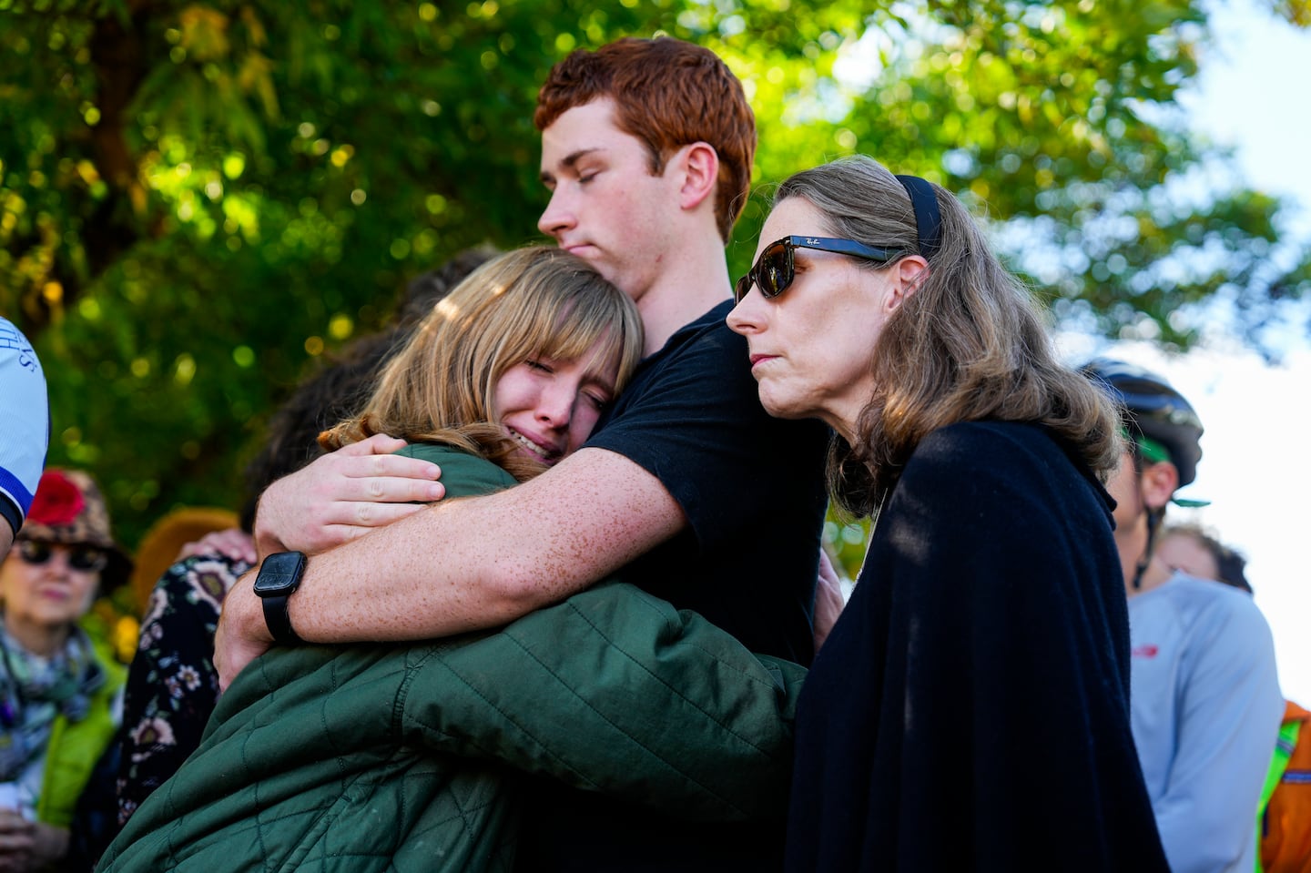 John Corcoran’s family (left to right) children, Christi and Jack, and wife, Barbara hugged after Ghost Bike ceremony held by cyclists and bike safety advocates on Sept. 28, 2024 on Memorial Drive.