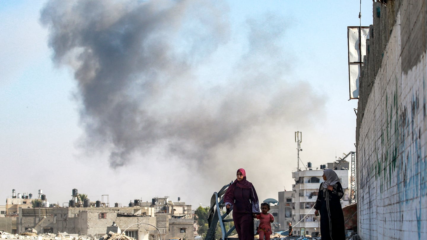 A woman walks with a child as smoke from Israeli bombardment rises in an area that was ordered to be evacuated by the Israeli army in the southeast of Khan Yunis in the southern Gaza Strip on Sept. 8.