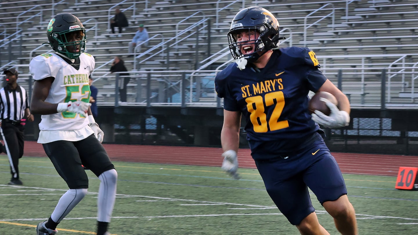 St. Mary's lineman Jake Peterson is all smiles after completing his pick-six return on the second play from scrimmage, setting the Spartans on their way to a big win over Jesiah Mack (left) and Cathedral Friday at the Manning Bowl in Lynn.