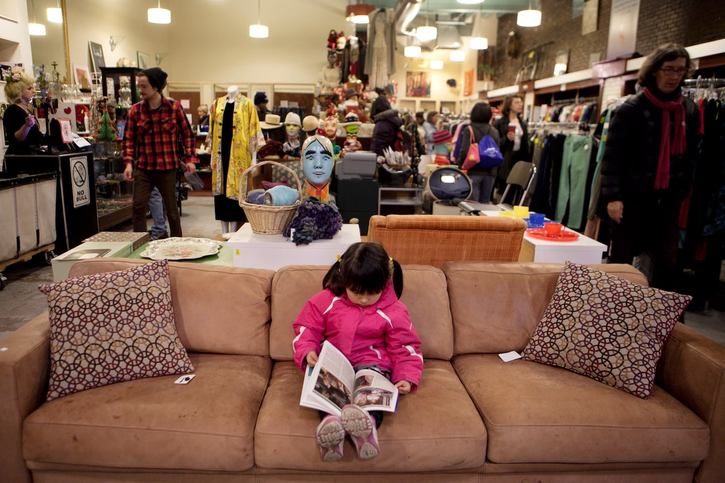 A child read a book while her mother shopped at the Boomerangs thrift store in Cambridge in 2013.