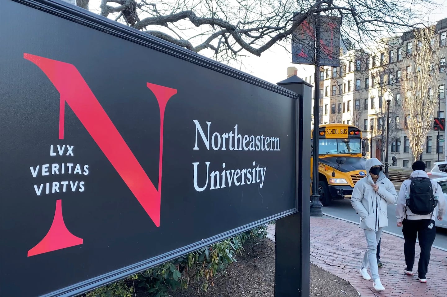 Pedestrians walk near a Northeastern University sign on the school's campus in Boston.