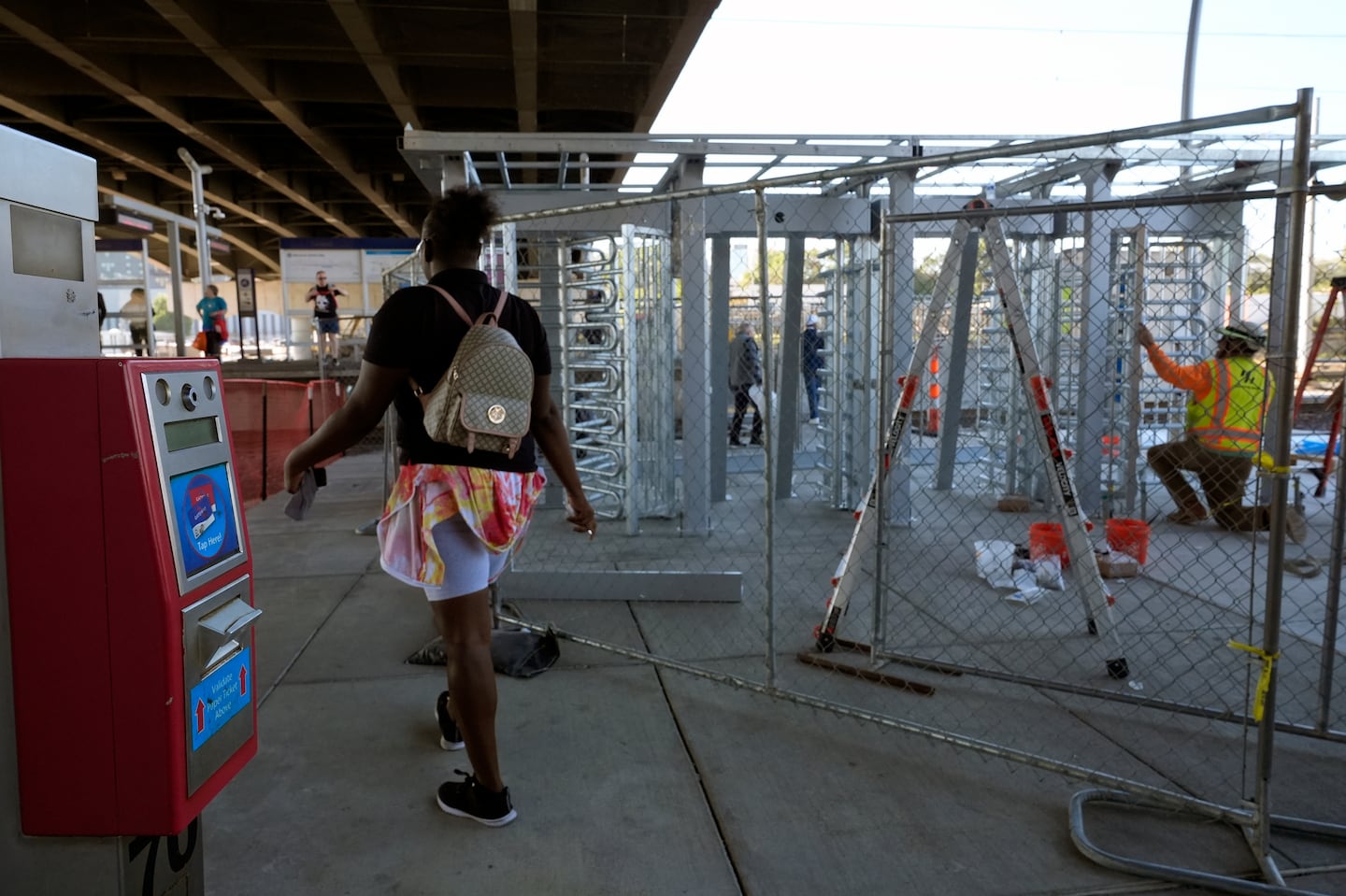 A rider passes a ticket validation scanner as workers install a metal gate that will prevent customers from entering a MetroLink platform without a valid fare card in an effort to increase security, on Oct. 9, in St. Louis.