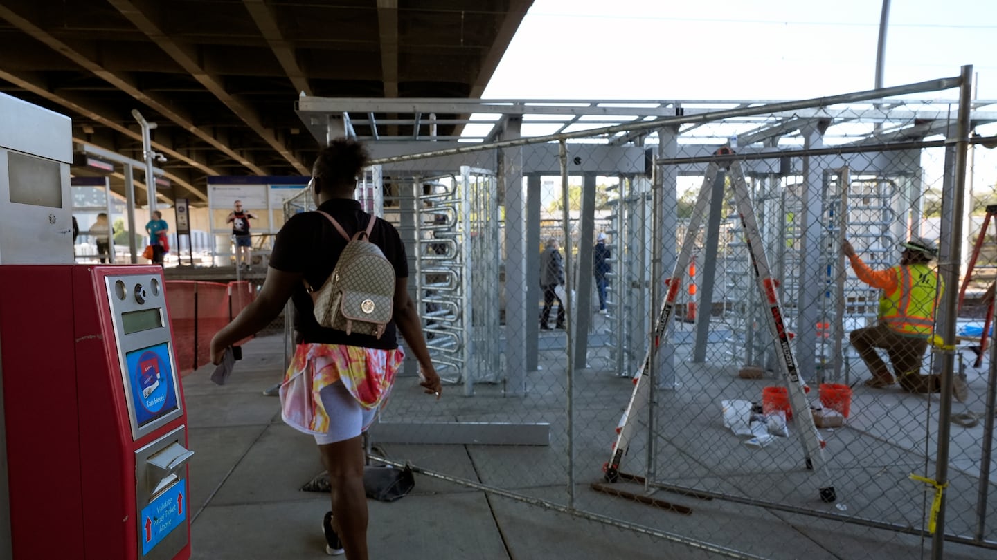 A rider passes a ticket validation scanner as workers install a metal gate that will prevent customers from entering a MetroLink platform without a valid fare card in an effort to increase security, on Oct. 9, in St. Louis.