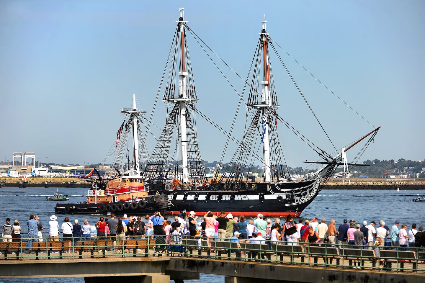 Spectators line the pier off Castle Island as they watch the USS Constitution, the nation’s oldest commissioned warship.