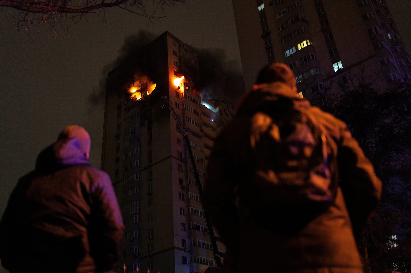 People look at Ukrainian firefighters working to put out a fire in a high-rise residential building after being reportedly hit by a drone, in Kyiv, on October 25, 2024, amid the Russian invasion on Ukraine.