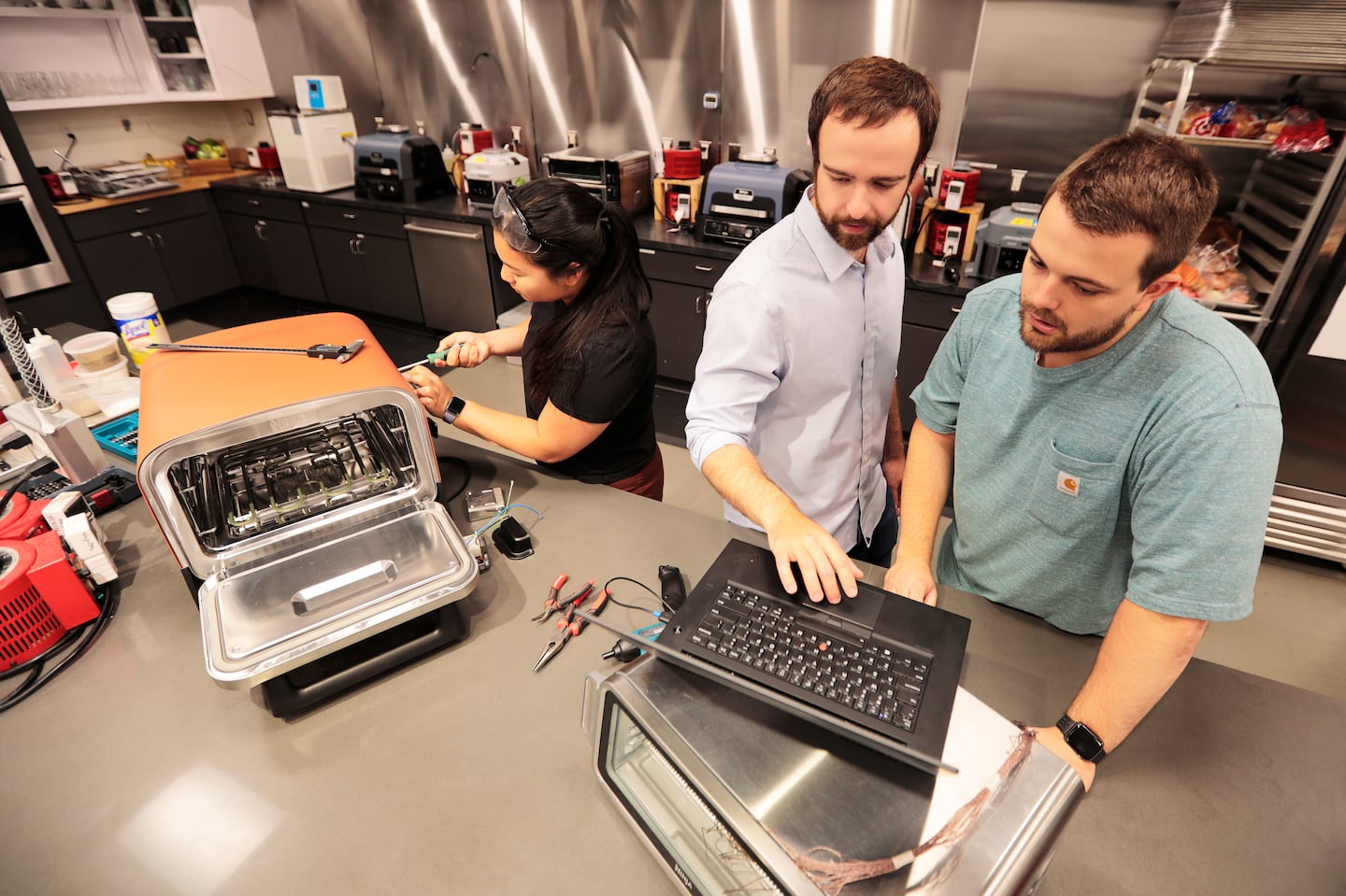 Mechanical engineers work in the SharkNinja test kitchen in this 2023 photo. Grace Sperling, left, works with outdoor heated appliances. Sean Dorsey, center, and Conor Dykeman work on indoor heated appliances.