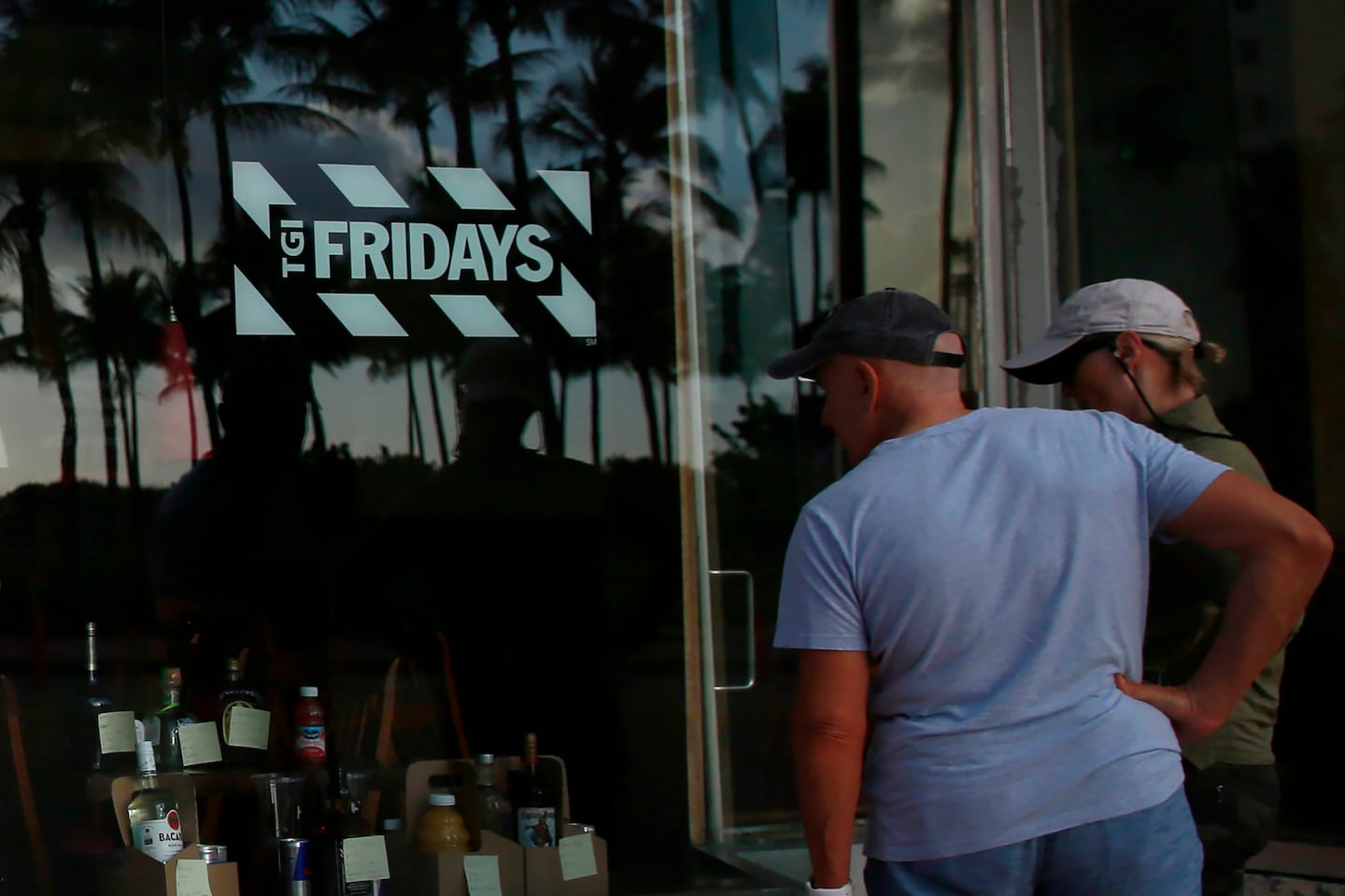 People peek into a window of a TGI Friday's restaurant to see what they are serving to-go on Wednesday, March 25, 2020, in Miami Beach, Fla.