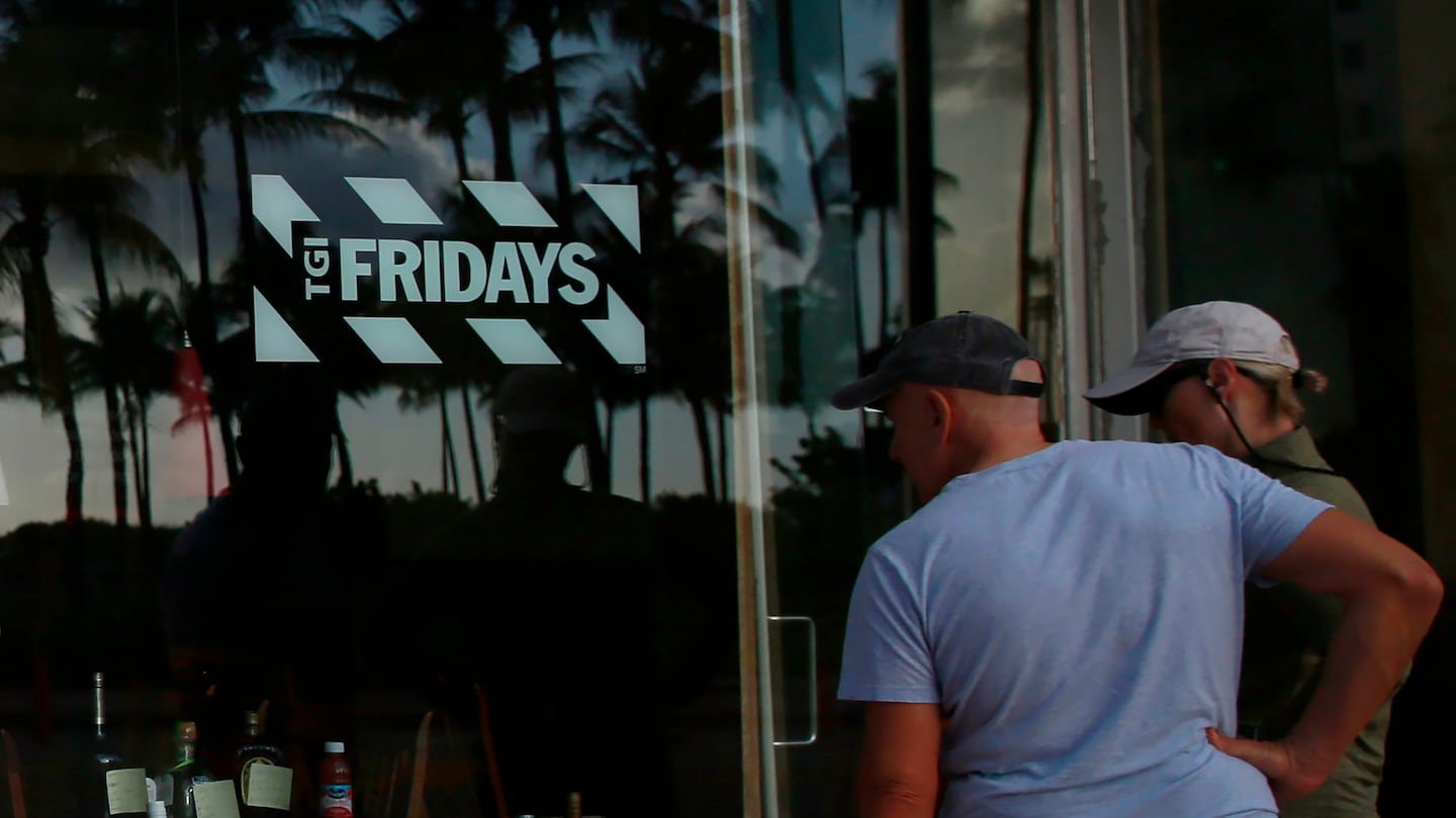 People peek into a window of a TGI Friday's restaurant to see what they are serving to-go on Wednesday, March 25, 2020, in Miami Beach, Fla.