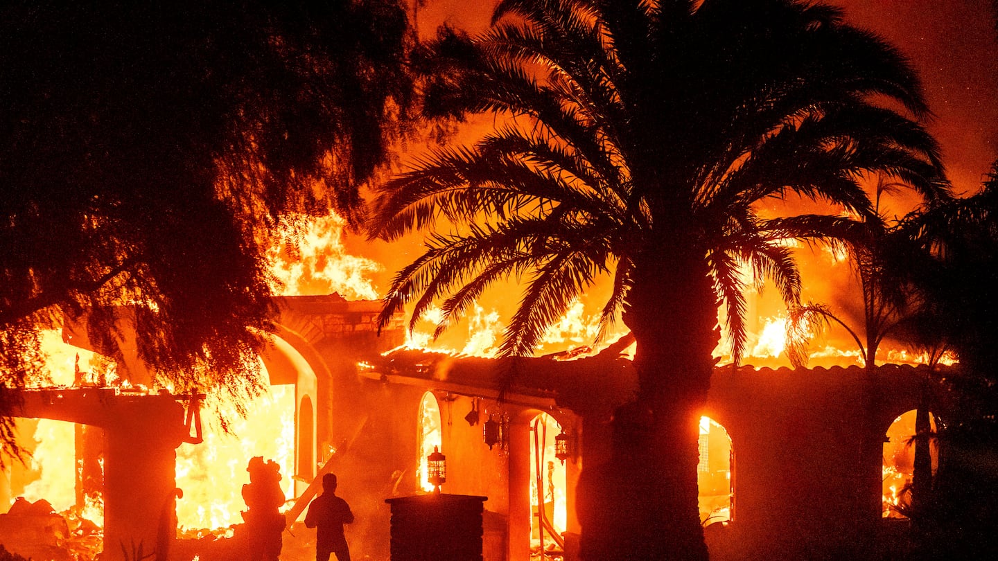 Television reporters film as flames from the Mountain Fire consume a home in Camarillo, Calif., on Nov. 6.