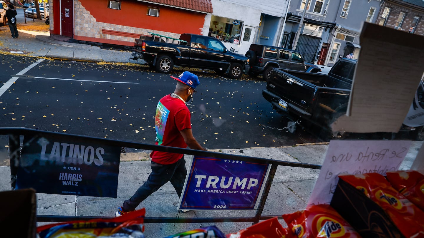 Campaign signs for both Trump and Democratic candidates were hung outside a Dominican-owned bodega in Reading, Pa., where shifting Latino political allegiances have become a key factor in Pennsylvania's battleground status. A pedestrian wearing a Puerto Rican flag baseball cap walked past the mixed political messaging, illustrating the divided loyalties in a city where Hispanic residents make up 68.9 percent of the population.