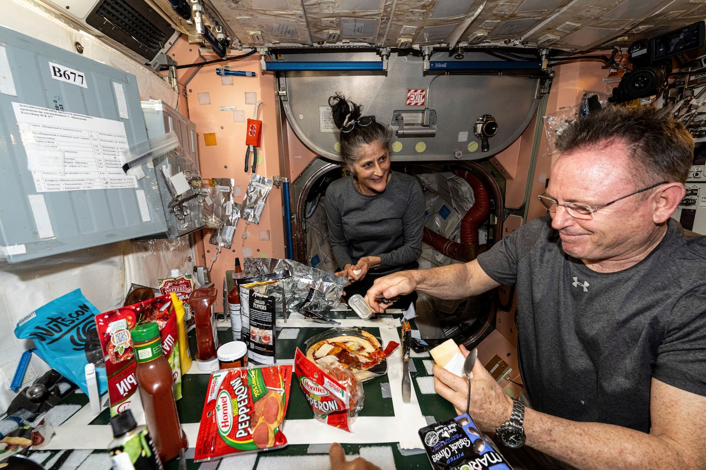 In this image released by NASA, NASA astronauts Suni Williams and Butch Wilmore, both Expedition 71 Flight Engineers, make pizza aboard the International Space Station's galley located inside the Unity module on Sept. 9, 2024. Items are attached to the galley using tape and velcro to keep them from flying away in the microgravity environment.