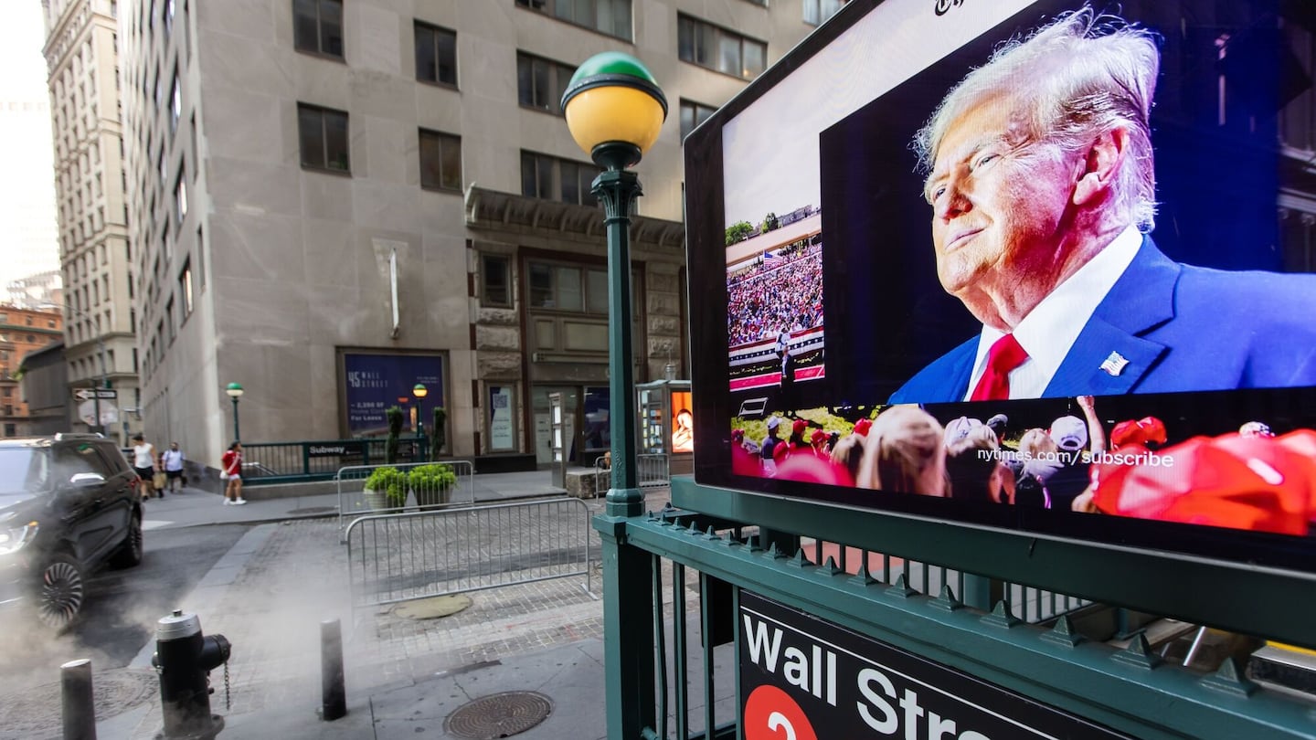 A screen displays an image of Donald Trump at a Wall Street subway station.