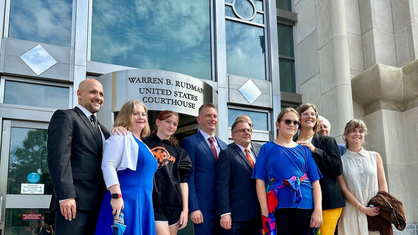 Two teens challenging New Hampshire's new law banning transgender girls from girls' sports teams, Parker Tirrell, third from left, and Iris Turmelle, sixth from left, pose with their families and attorneys in Concord, N.H., Monday, Aug. 19, 2024.