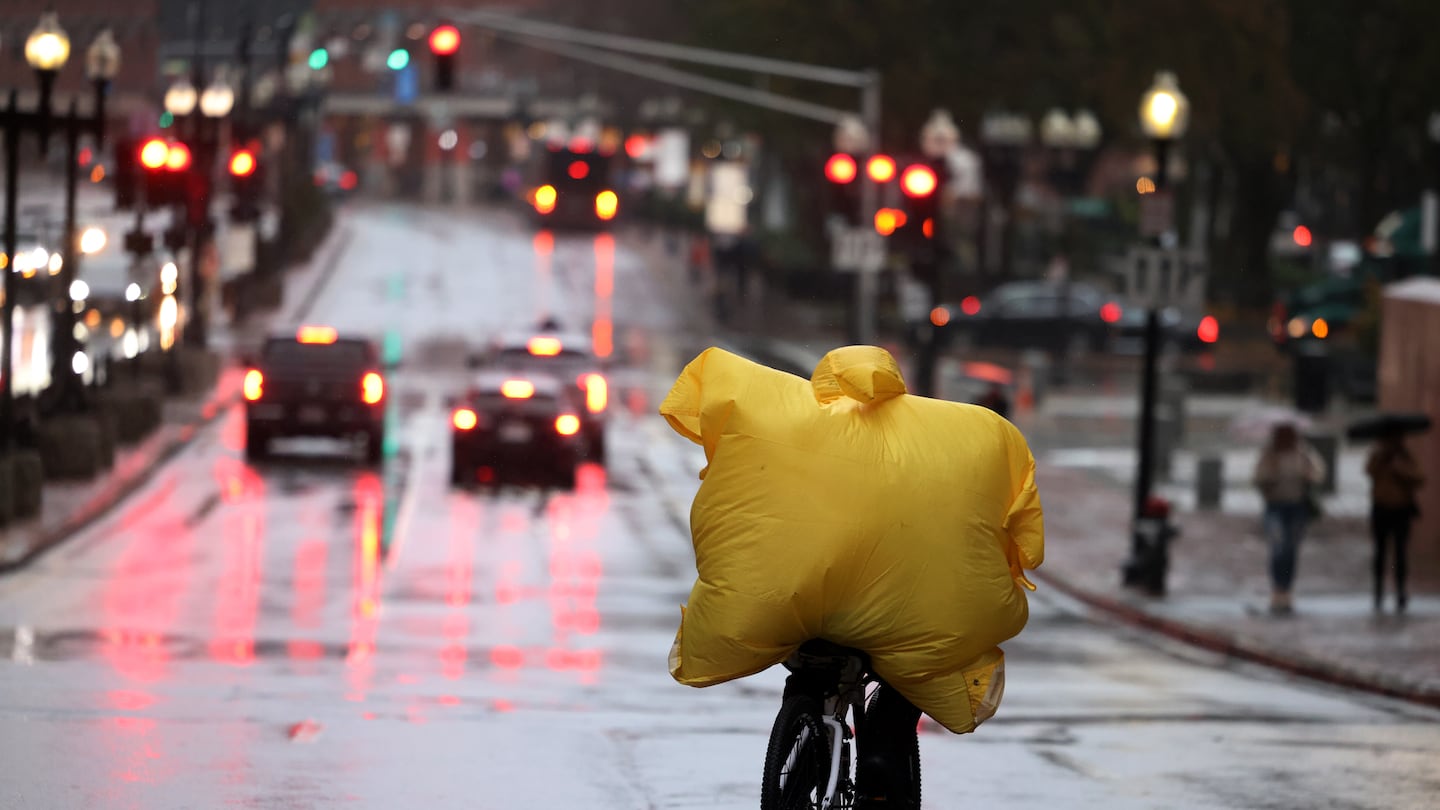 The wind puffs up a bicyclist’s poncho as he makes his way down Congress Street as the rain fell in Boston Thursday.