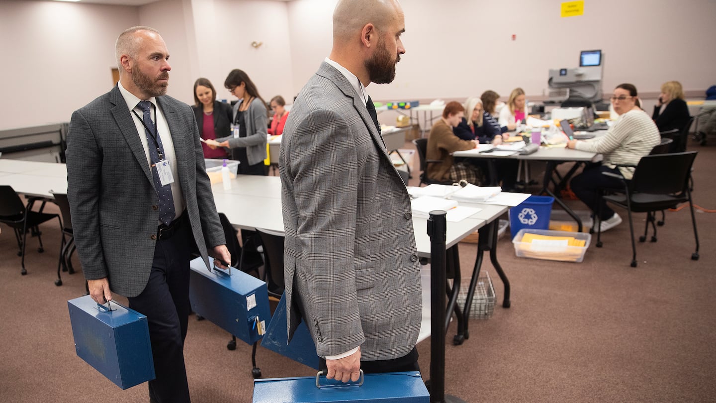 Detectives Dustin Tierney and David Silk, right, of the Department of the Secretary of State carry ballot boxes into the tabulation room on Nov. 14, in Augusta, Maine.