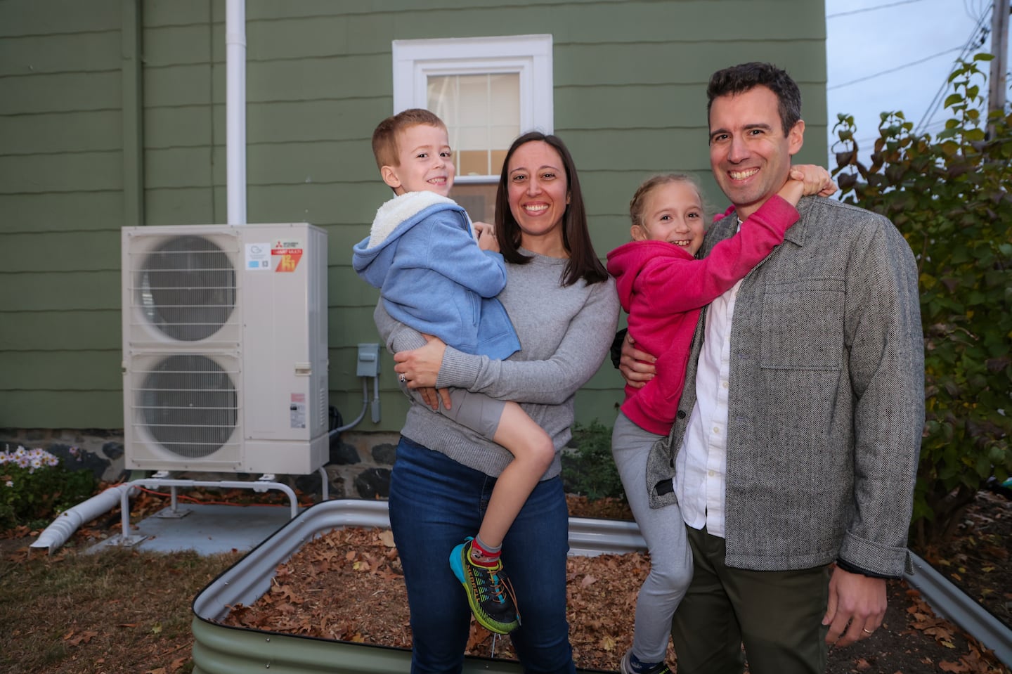 Tim Maher, Amelia Wesselink, and their children, Ayla, 8, and Otto, 5, in front of the HVAC system outside their Roslindale home after they installed an air-source heat pump last year.