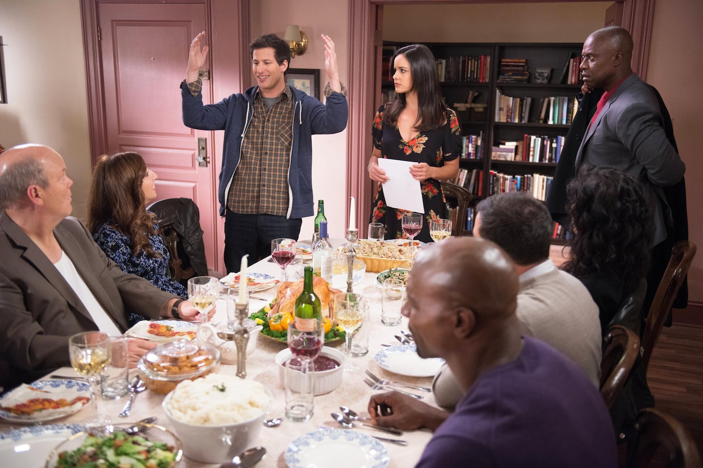 Det. Jake Peralta (Andy Samberg, third from left) and Capt. Ray Holt fourth from right) are dispatched during Det. Amy Santiago's (Melissa Fumero, center) holiday dinner in an episode of "Brooklyn Nine-Nine."