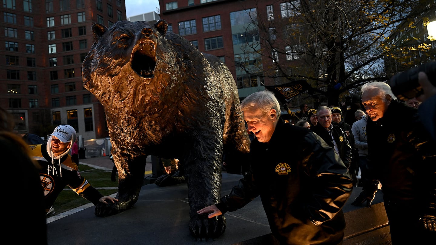 Bruins legend Bobby Orr (center), followed by Phil Esposito, touch the bear claw of the new commemorative statue to honor Bruins alumni and celebrate a century of Bruins hockey following a ceremony Saturday outside TD Garden.