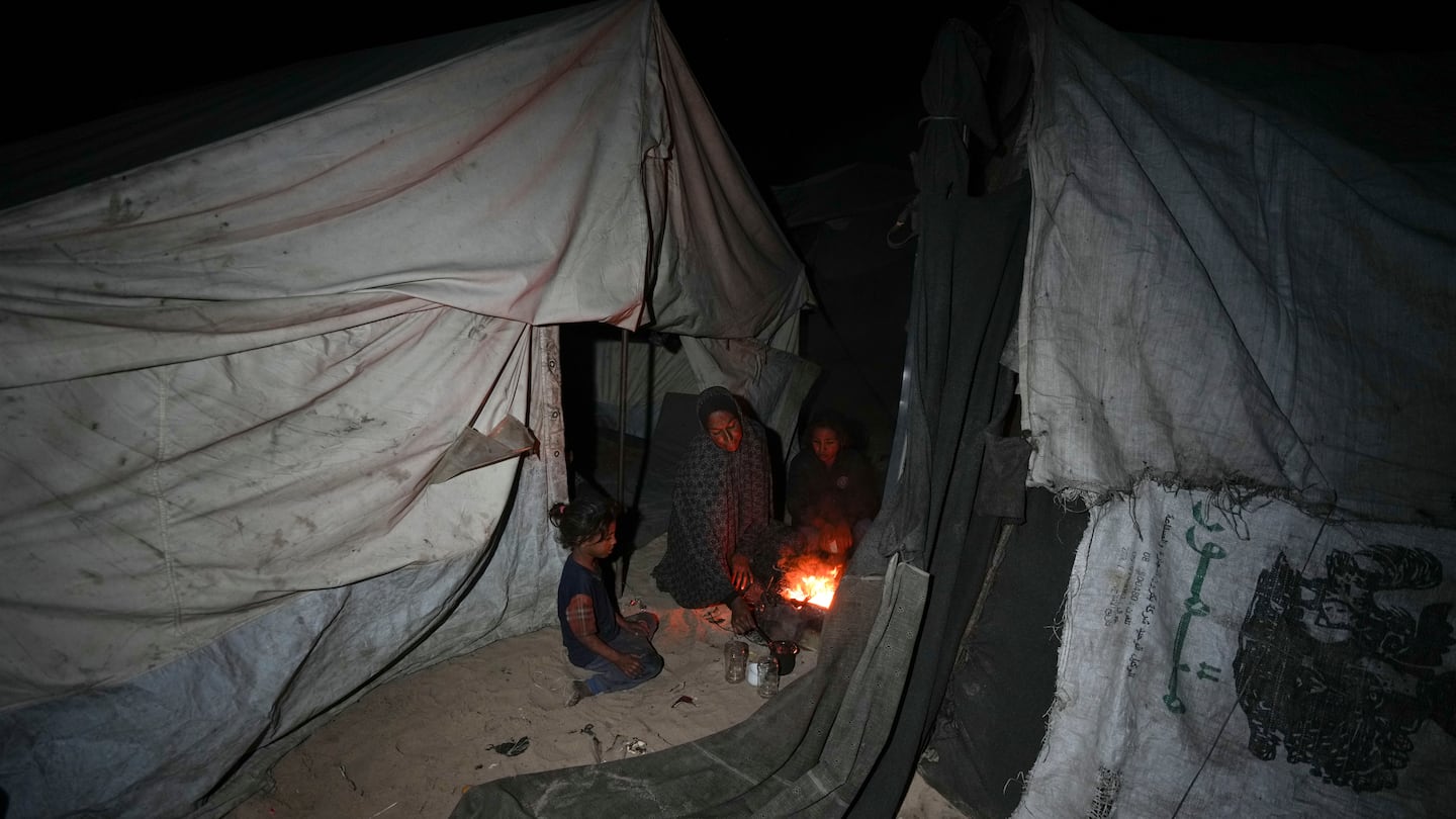 Shireen Daifallah, who was displaced with her children from northern Gaza, checks the fire next to their tent at a camp for displaced people in Deir al-Balah, Gaza Strip, on Nov. 30.