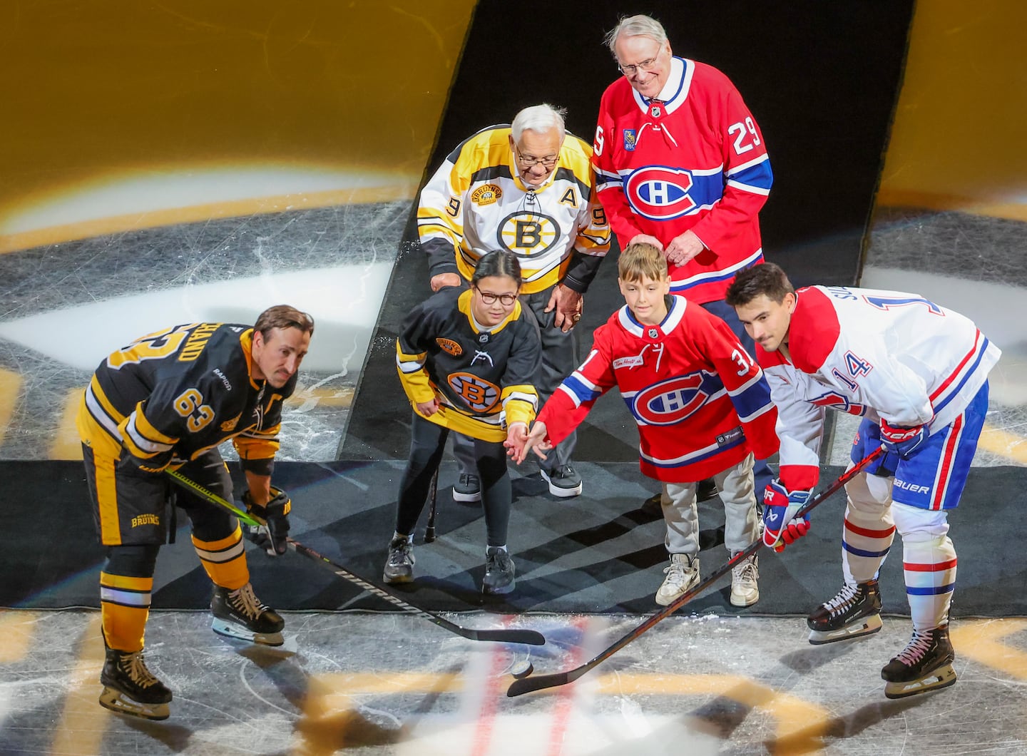 Former Bruin Johnny Bucyk (back left) and former Canadiens goalie Ken Dryden (back right) were once part of a heated Boston-Montreal rivalry but were all smiles during Sunday's puck drop between Bruins captain Brad Marchand (63) and Canadiens center Nick Suzuki (14) before Sunday's game marking 100 years of Bruins hockey.
  
