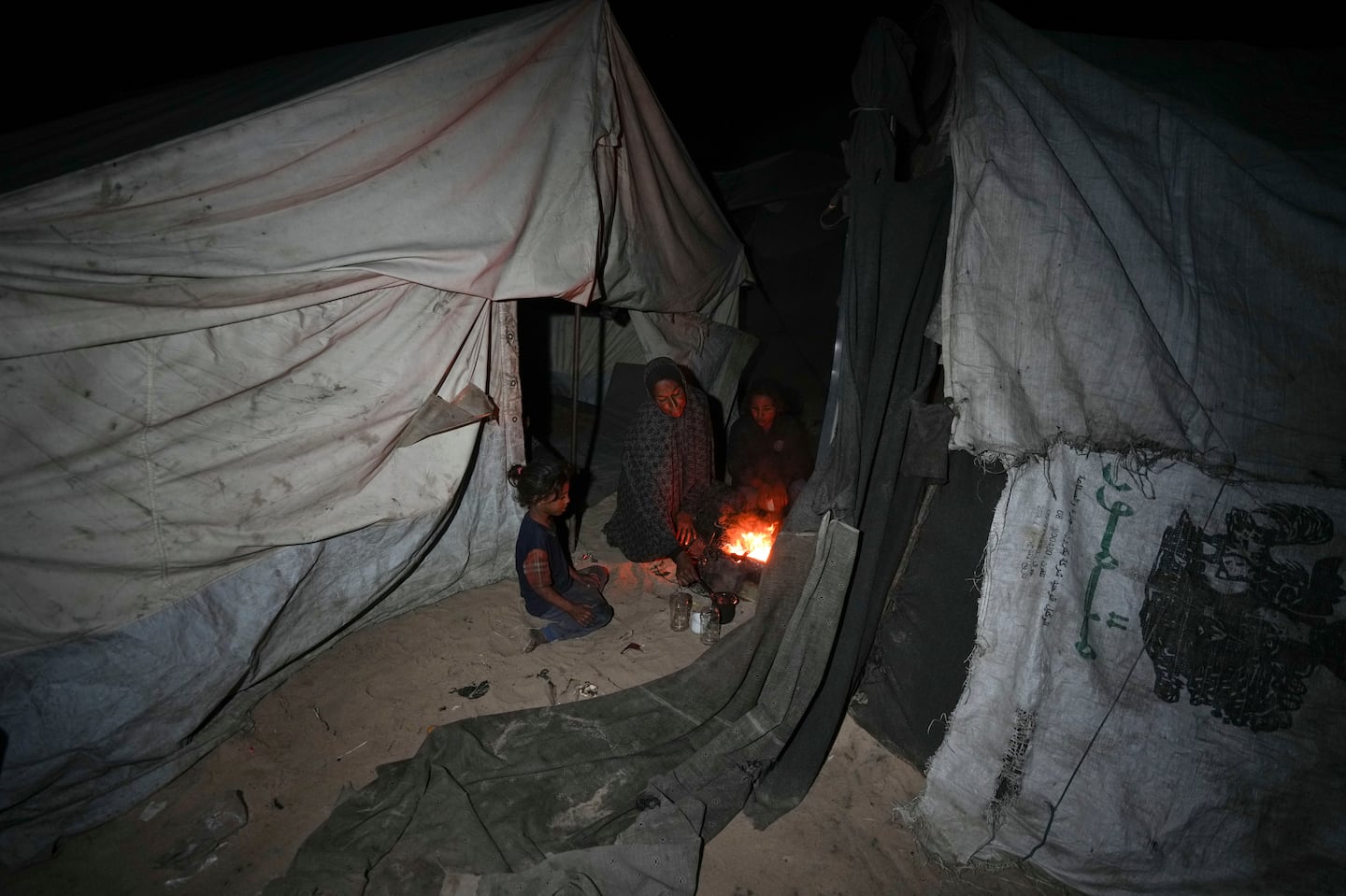 Shireen Daifallah, who was displaced with her children from northern Gaza, checks the fire next to their tent at a camp for displaced people in Deir al-Balah, Gaza Strip, on Nov. 30.