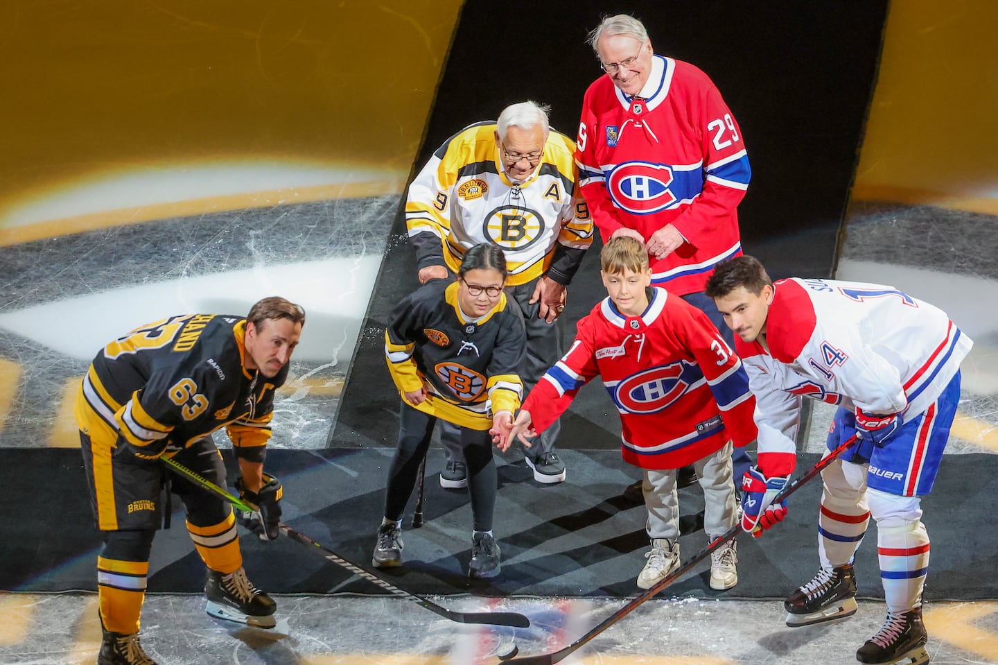 Former Bruin Johnny Bucyk (back left) and former Canadiens goalie Ken Dryden (back right) were once part of a heated Boston-Montreal rivalry but were all smiles during Sunday's puck drop between Bruins captain Brad Marchand (63) and Canadiens center Nick Suzuki (14) before Sunday's game marking 100 years of Bruins hockey.
  
