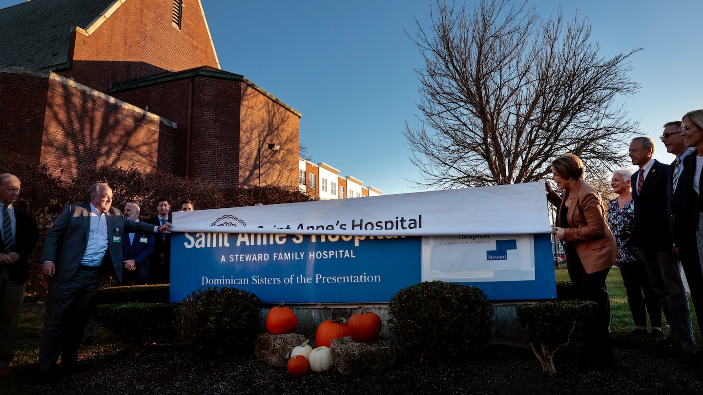 Brown University Health CEO John Fernandez (left), and Massachusetts Governor Maura Healey unfurled a Brown University Health banner for St. Anne's Hospital, covering the former Steward Family Hospital sign, during a ceremony at the Fall River hospital on Nov. 19.