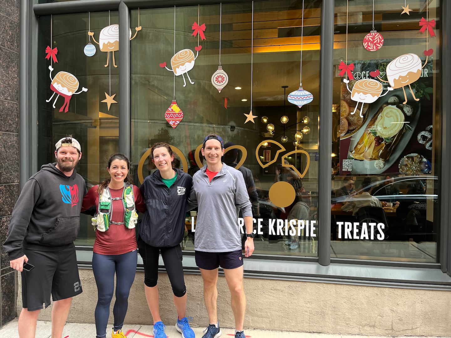 Runners take a photo in front of a Flour Bakery holiday window display in December 2023, the inaugural half marathon fun run.