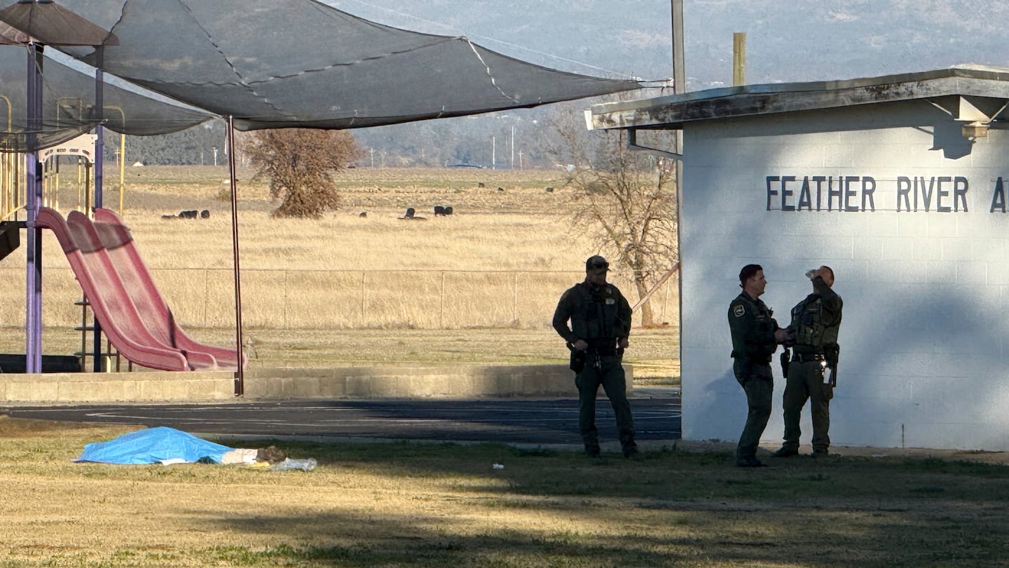 Police officers stand near a body covered by a tarp outside of Feather River Adventist School after a shooting, Dec. 4, in Oroville, Calif.