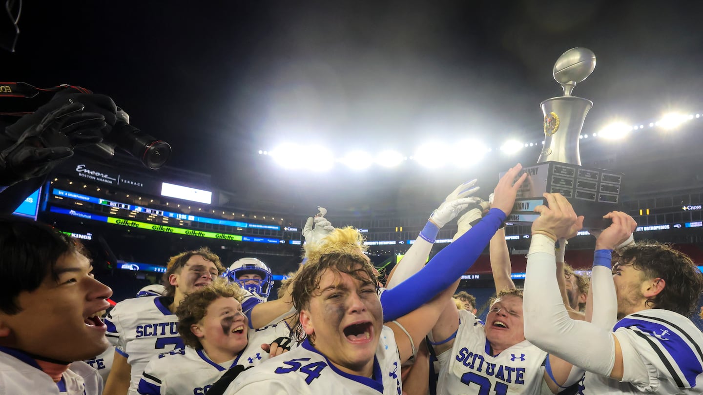 Scituate's Willy Robinson (21) holds up the Division 4 state championship trophy as Sean Coyne (54) is overcome with emotion.