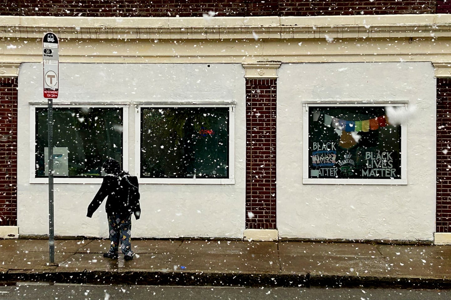 Large wet snowflakes fall on a commuter waiting at a bus stop in Roslindale on Thursday.