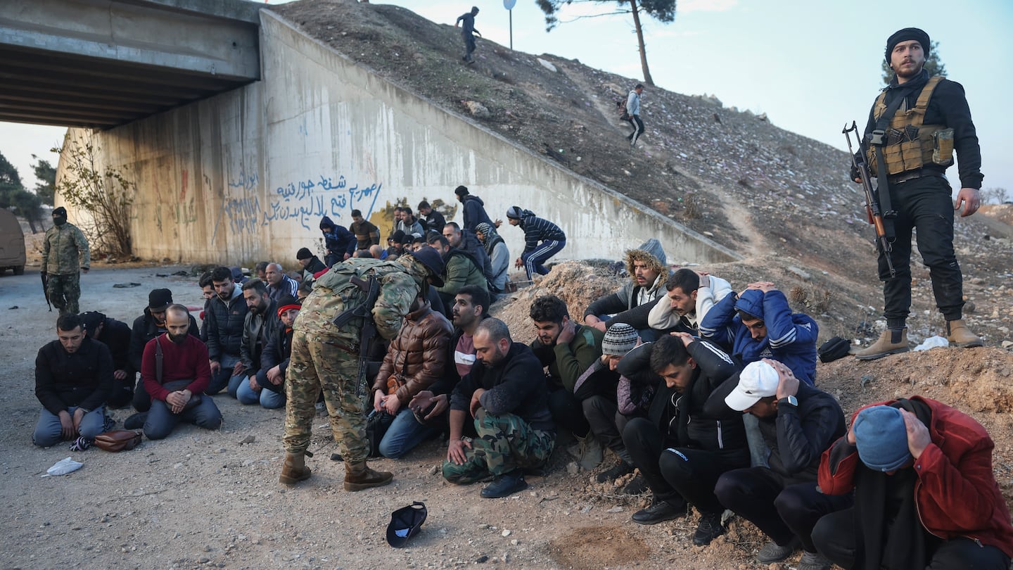 Government soldiers and allies sit on the floor as they are taken into custody by opposition fighters on the road between Homs and Damascus, near Homs, Syria, on Sunday, Dec. 8.