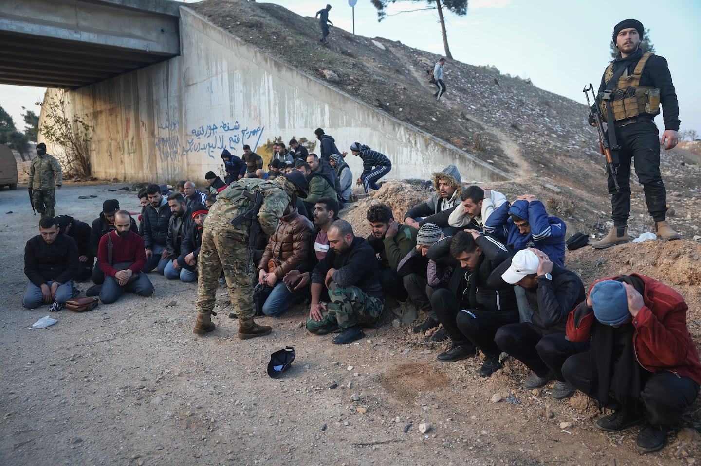 Government soldiers and allies sit on the floor as they are taken into custody by opposition fighters on the road between Homs and Damascus, near Homs, Syria, on Sunday, Dec. 8.