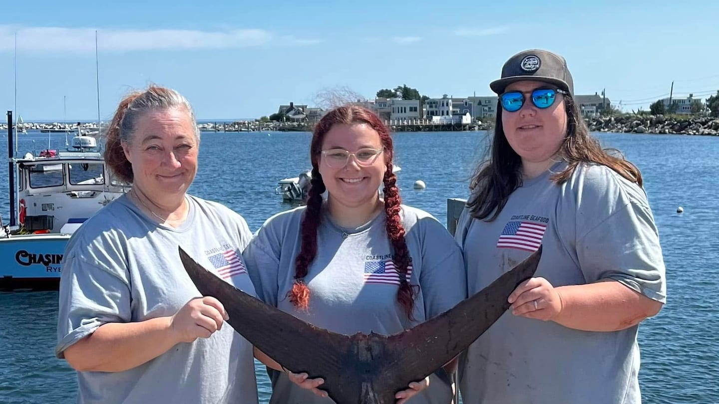 From left to right: Linda Hunt, Anabelle Sims-Hunt, and Denise Hunt stand with the tail of a fish. The three women operate a seafood company called Coastline Seafood together. :