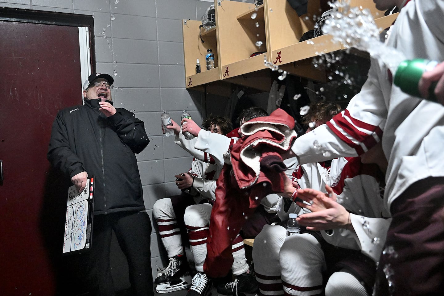 Arlington boys' hockey coach John Messuri gets sprayed with water by his players in the locker room after reaching his 400th career win at Ed Burns Arena.