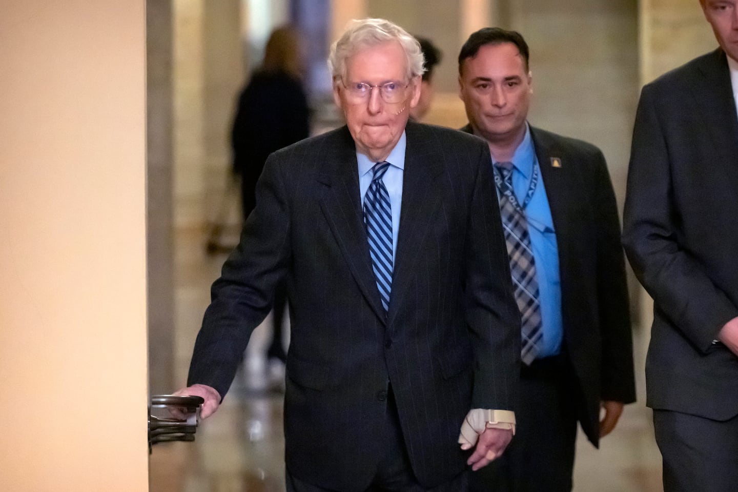 Senate Minority Leader Mitch McConnell of Ky., left, wears a bandage on his face and wrist as he walks to cast a vote on the Senate floor after falling during a luncheon on Capitol Hill.