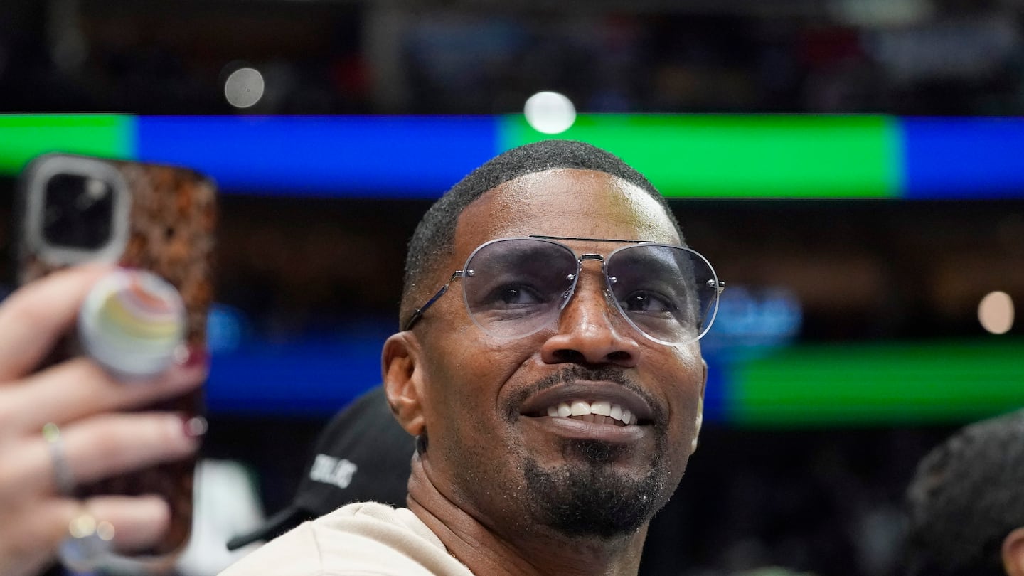 Jamie Foxx smiles during an NBA basketball game between the Washington Wizards and Dallas Mavericks in Dallas, Saturday, Nov. 27, 2021.