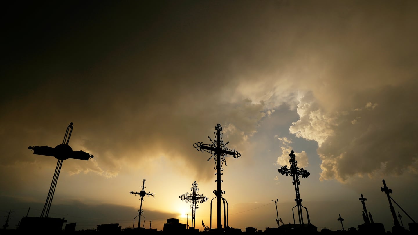 Iron crosses marking graves are silhouetted against storm clouds building over a cemetery, May 25, in Victoria, Kan.