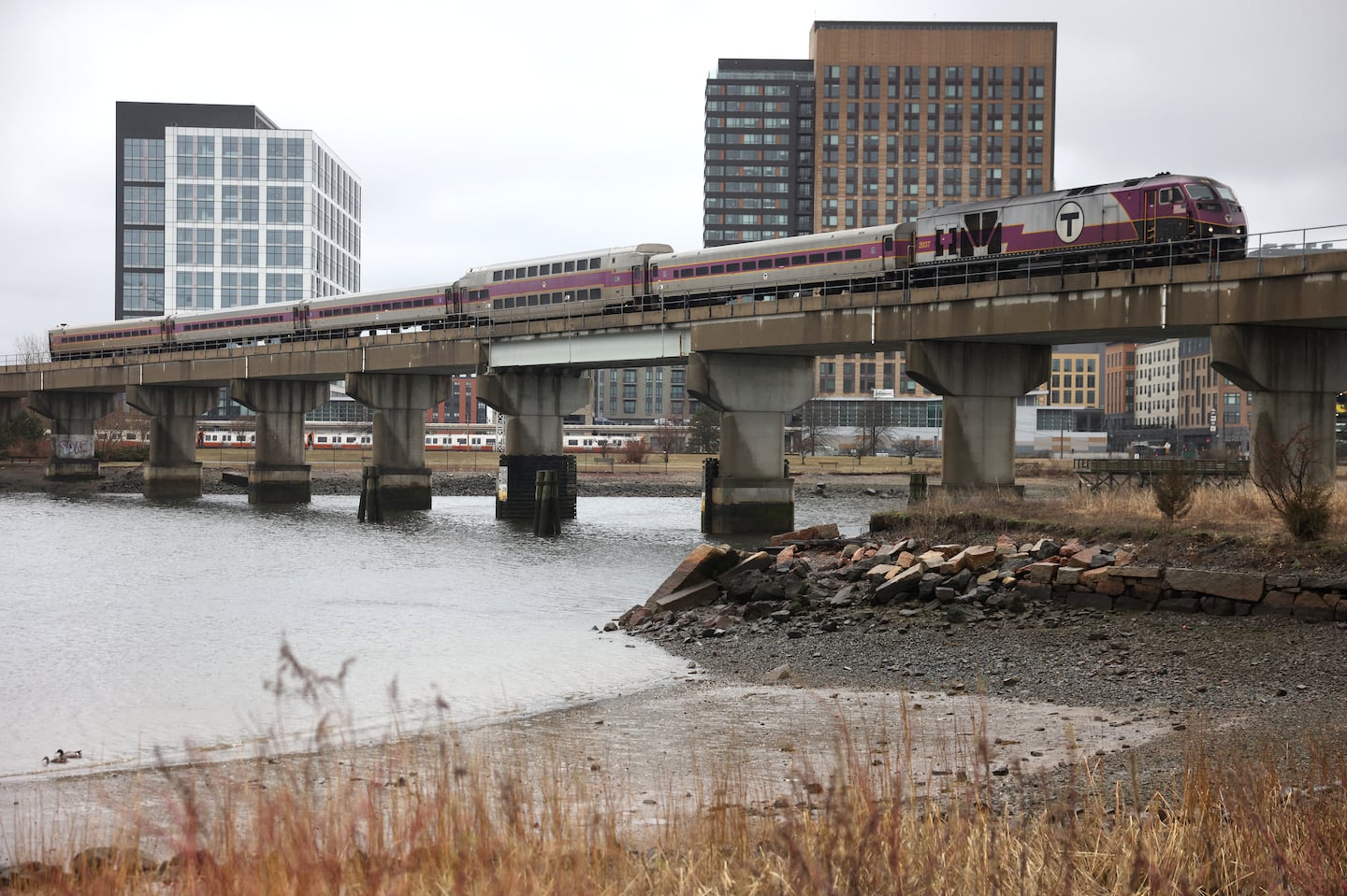 A commuter rail train passes over a bridge above a the location of a proposed bridge between Everett and Somerville.