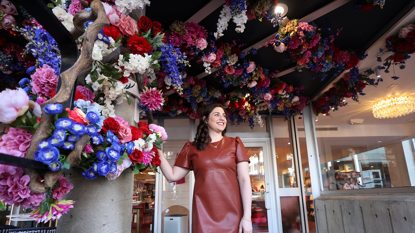 Rachel Kanter stands under the silk flowers at the entrance to her new store, Lovestruck Books, in Harvard Square.