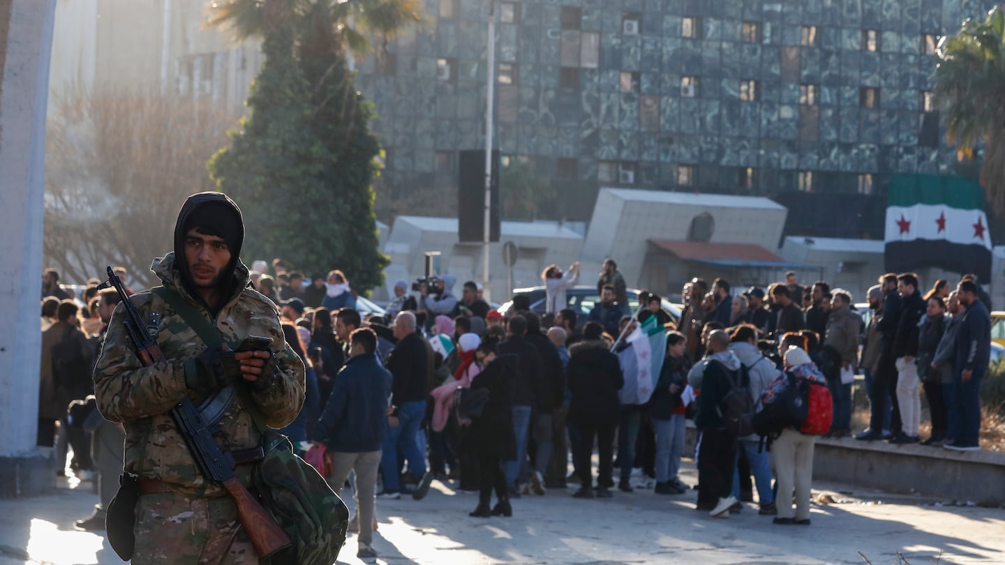 A Syrian fighter stands guard as activists gather at the Umayyad square during a protest to demand a secular state, in Damascus, Syria, on Dec. 19.