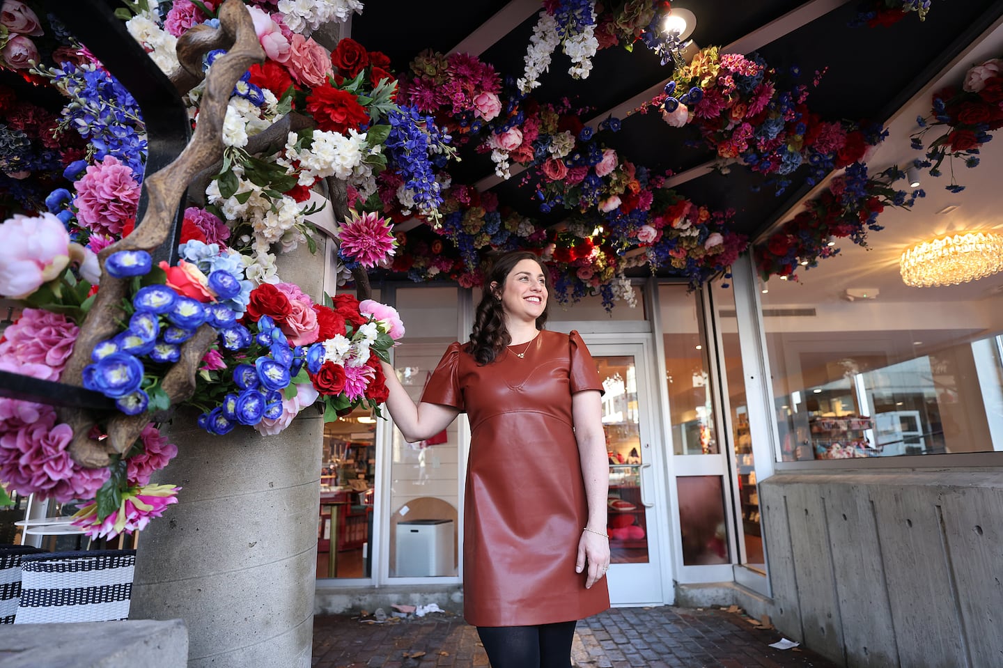 Rachel Kanter stands under the silk flowers at the entrance to her new store, Lovestruck Books, in Harvard Square.