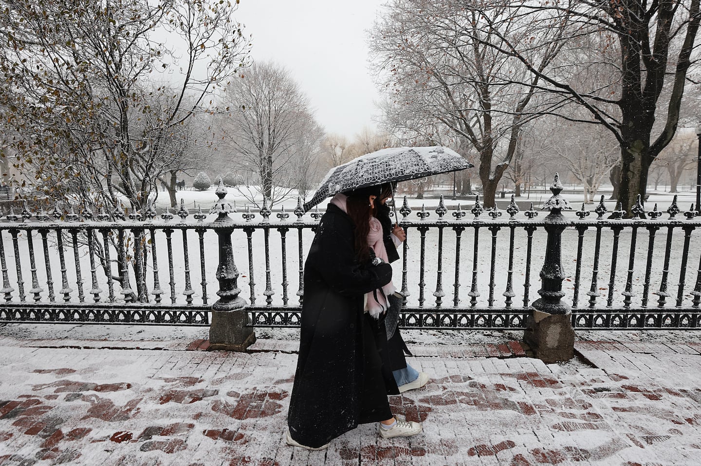 Two people shared an umbrella as they walked past a snowy Public Garden in Boston on Friday.